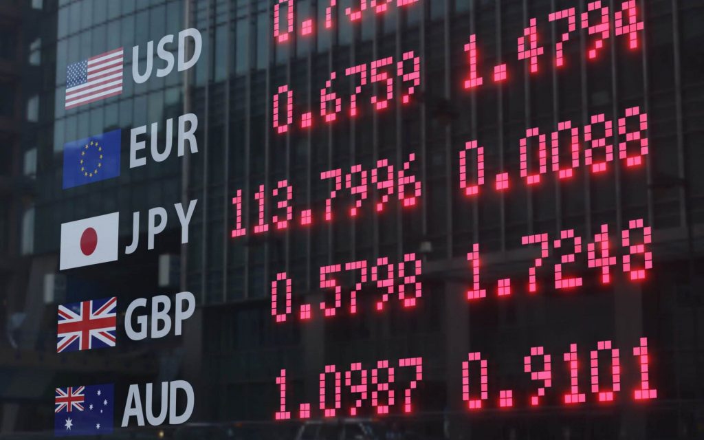 A digital board showing foreign exchange rates behind a window glass reflecting commercial buildings. Illustration of the concept of FOREX, currency trading and monetary policies